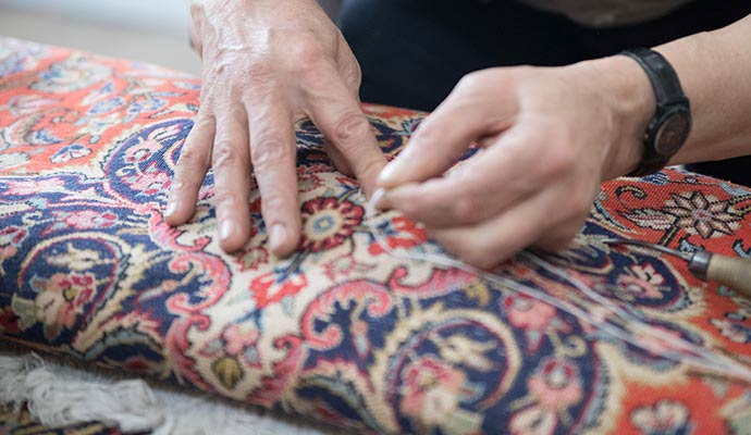 Close up of a skilled craftsman hand stitching a traditional oriental rug during restoration